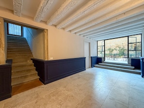Een trap die leidt naar een plateau met een donker houten afwerking, een groot raam met uitzicht op terrasmeubilair, en een stenen muur.