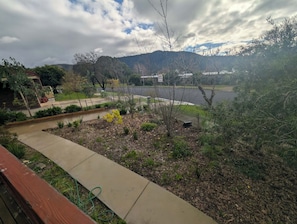 Un jardín ajardinado con un sendero, un pequeño estanque y vistas a una colina con edificios al fondo.
