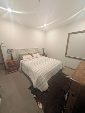 A bedroom with a bed, nightstands, a wooden desk, and a large mirror.