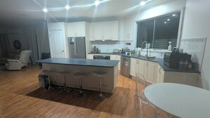 A modern kitchen with a central island, bar stools, a dining table, and a large window.
