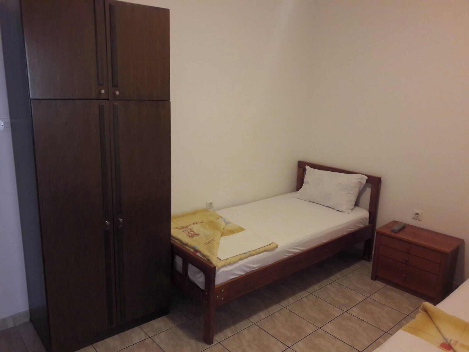 Une petite chambre à coucher avec un lit simple, une armoire en bois, une table de chevet et une commode.