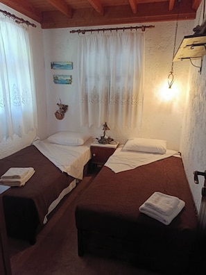 A room with two beds, a nightstand with a lamp, a wall clock, and a hanging light fixture.