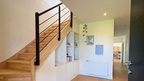 Un interno moderno con una scala in legno, scaffalature integrate bianche, un termosifone e un tappeto colorato.