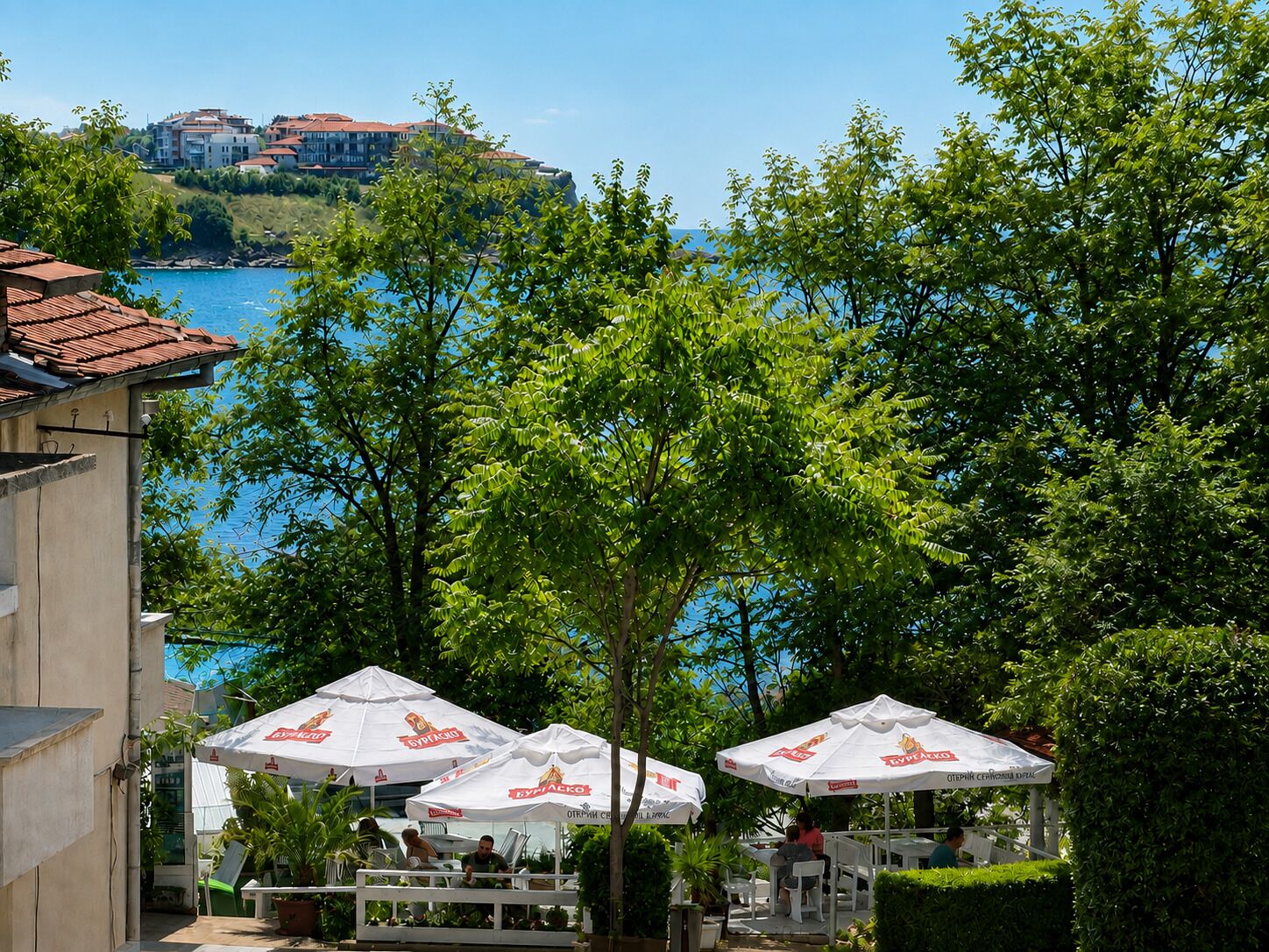 Outdoor seating with umbrellas, a view of the sea, and buildings in the background.