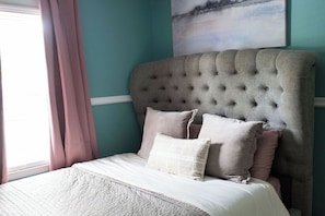 Une chambre à coucher avec une tête de lit capitonnée, un lit recouvert de linge de lit blanc et un mur de couleur turquoise.