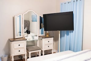 Ein Schlafzimmer mit einem Bett, einer Kommode mit Schubladen, einem Schminktisch mit Spiegel und einem an der Wand befestigten Flachbildfernseher.