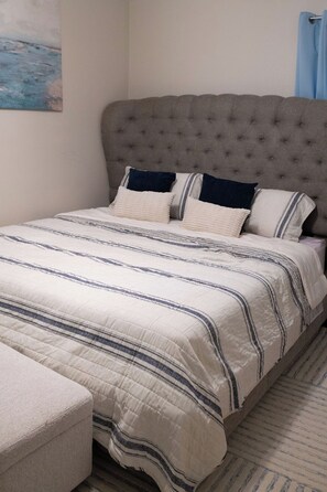 Ein Schlafzimmer mit einem gesteppten Kopfteil, einem Bett mit gestreifter Bettwäsche und einem passenden Hocker.