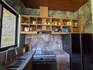Uma cozinha com painel de pedra, prateleiras de madeira, forno embutido e geladeira.
