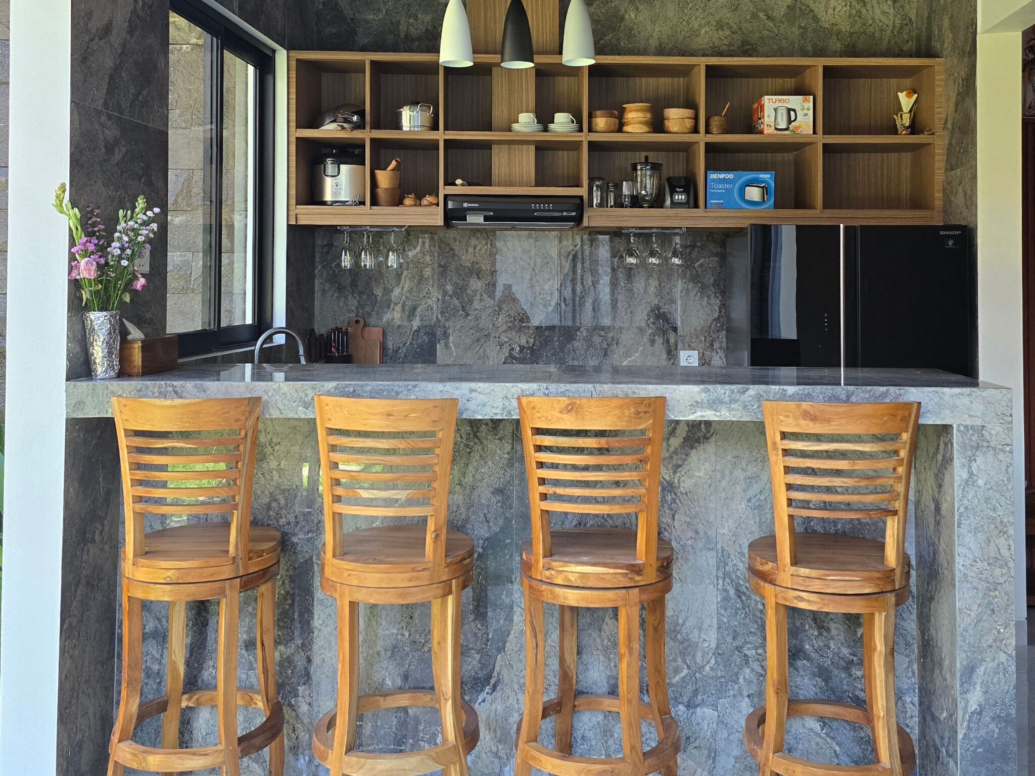 Una cocina con estantes de madera, cafetera, tostadora y tres taburetes de bar de madera.