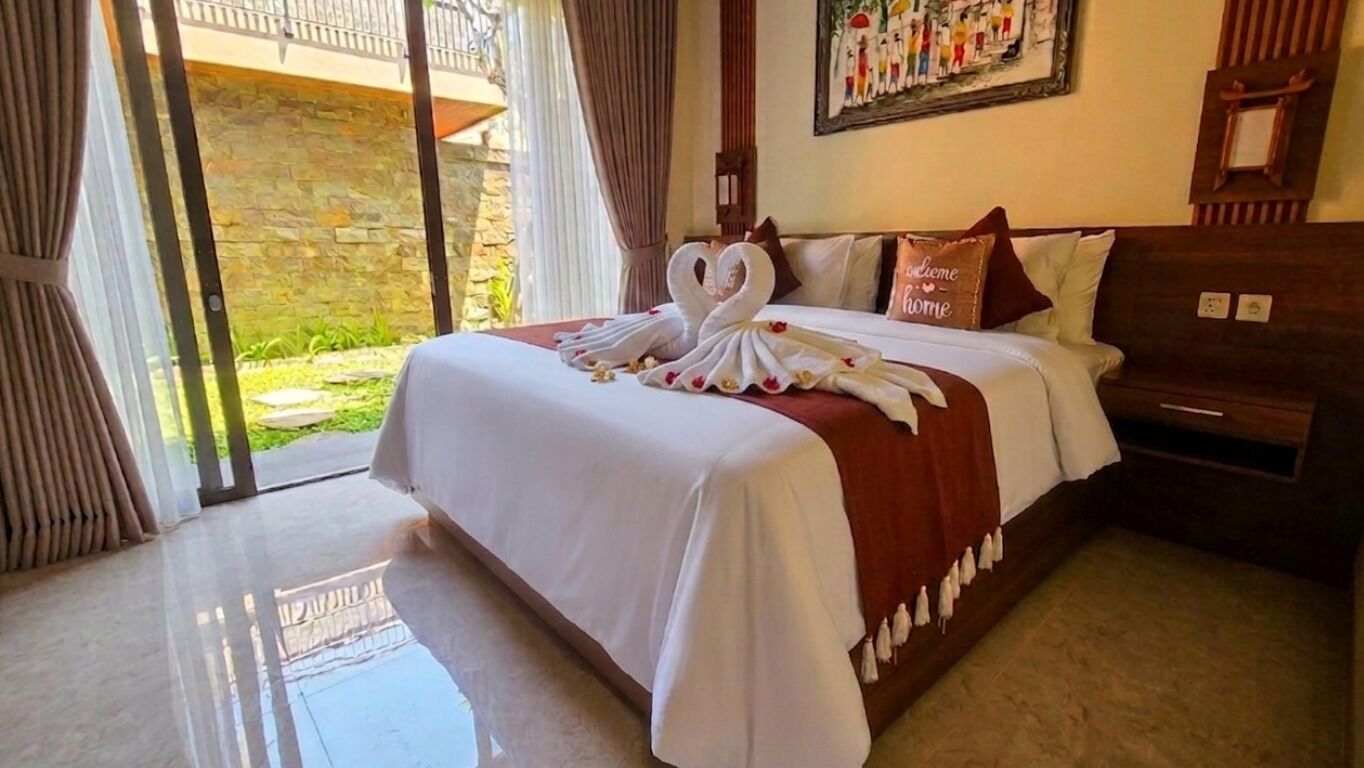 A hotel room with a bed, a wooden headboard, a painting on the wall, and a view of the outdoors through a glass door.