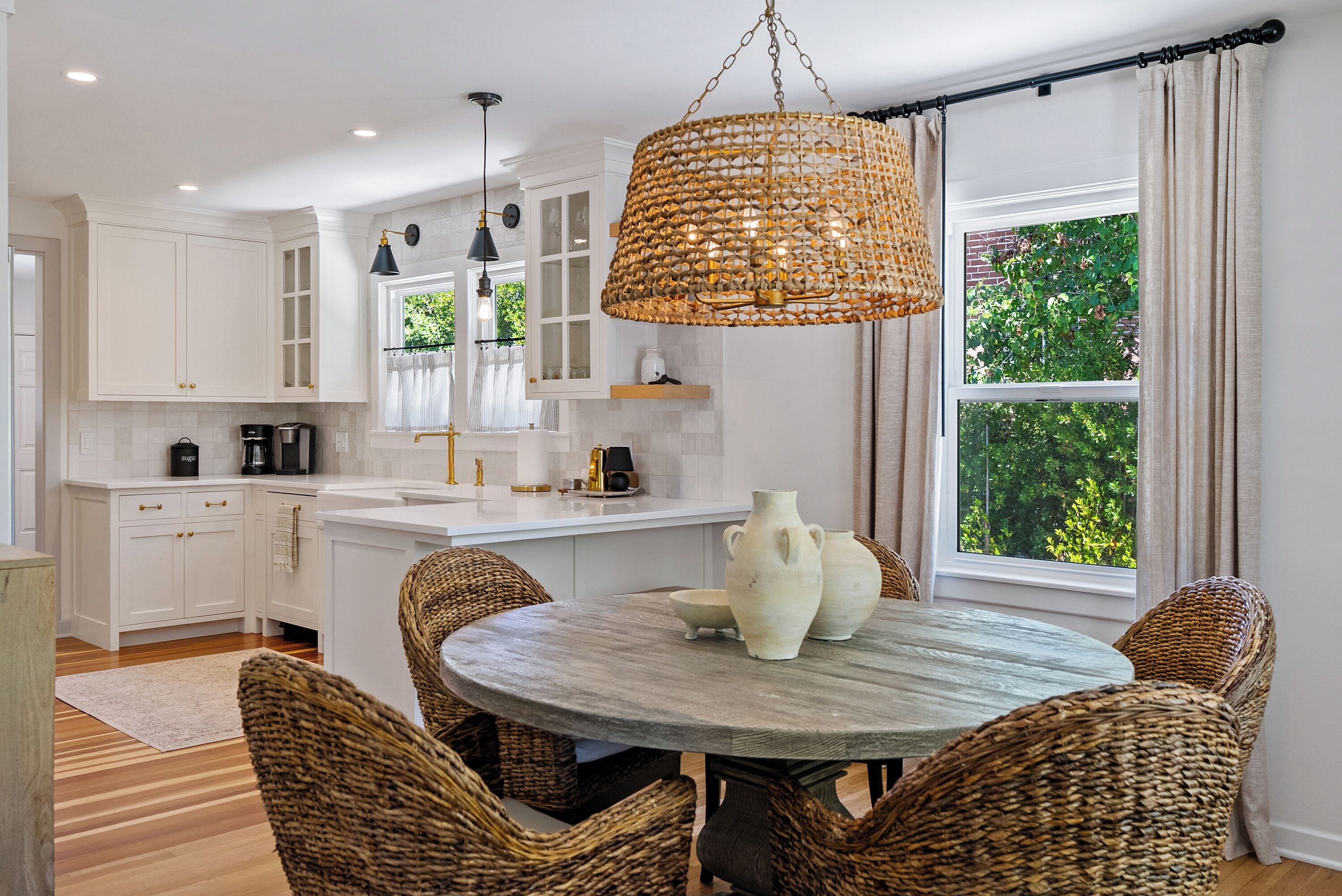 A modern kitchen with white cabinetry, a dining table with wicker chairs, and a large woven pendant light.