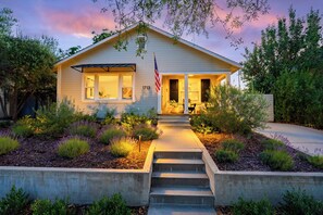A single-story house with a front porch, a flag, and a number '1713' on the wall. - Lavender Porch - Designer Bungalow with Fire Pit Near Downtown Paso (Paso Robles)