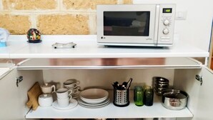 A kitchen with a microwave on the countertop, a shelf with dishes, and a box on the lower shelf. - Just minutes from the city, perfect for everyone—including families with kids (play area) (Bari)