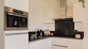 Una cocina moderna con horno empotrado, electrodomésticos de acero inoxidable, armarios blancos y encimera negra.