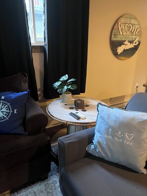 Ein gemütliches Wohnzimmer mit einem runden Couchtisch, einer Zimmerpflanze, einer Wanduhr und einem dekorativen Wandbild.
