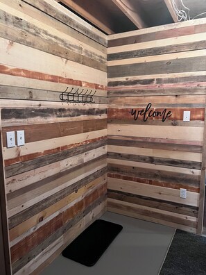 A room with a slatted wooden wall, a black mat on the floor, and a 'welcome' sign. - Charmer Down Under (Kentville)