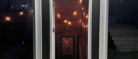 Una pequeña construcción de madera con entrada abierta, un cartel que indica Airbnb y una terraza de madera al frente.