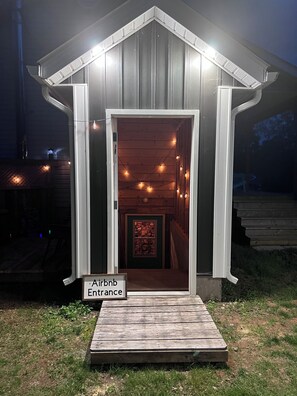 Ein kleines Holzgebäude mit offenem Eingang, einem Schild mit der Aufschrift Airbnb und einer hölzernen Terrasse davor.