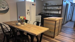 Eine Küche mit Kühlschrank, einem Holzespeisetisch mit Stühlen, einer kleinen Kochinsel mit Schubladen und einem Regal mit Geschirr.