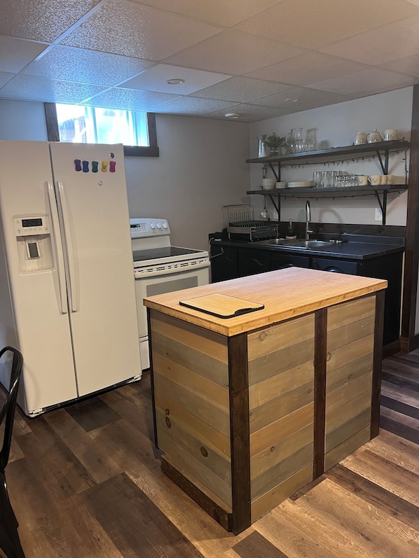Una cocina con refrigerador, estufa, una isla de madera y estantes con vajilla.