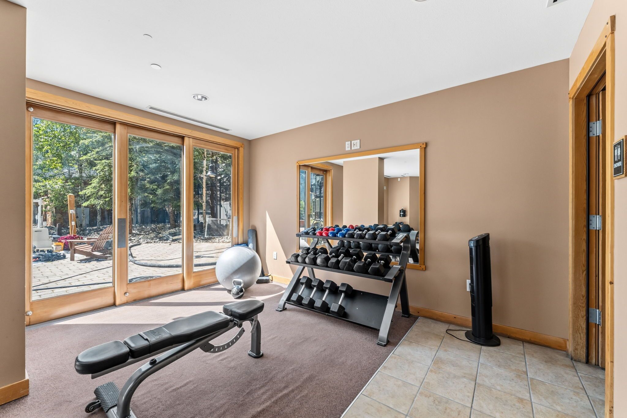 Un gimnasio con equipo de ejercicio, un espejo y ventanas amplias.