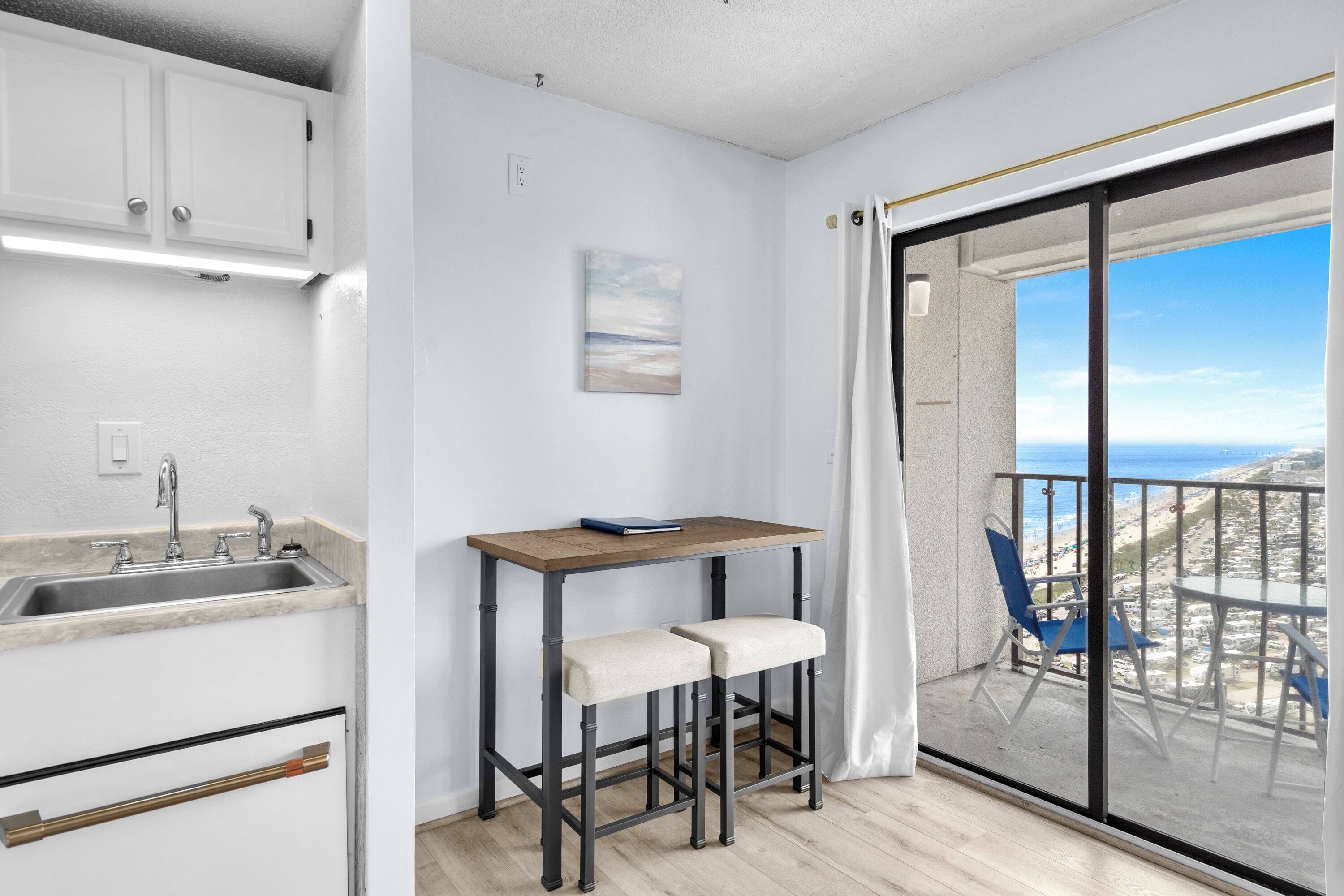 A balcony with a view of the beach and parked cars.