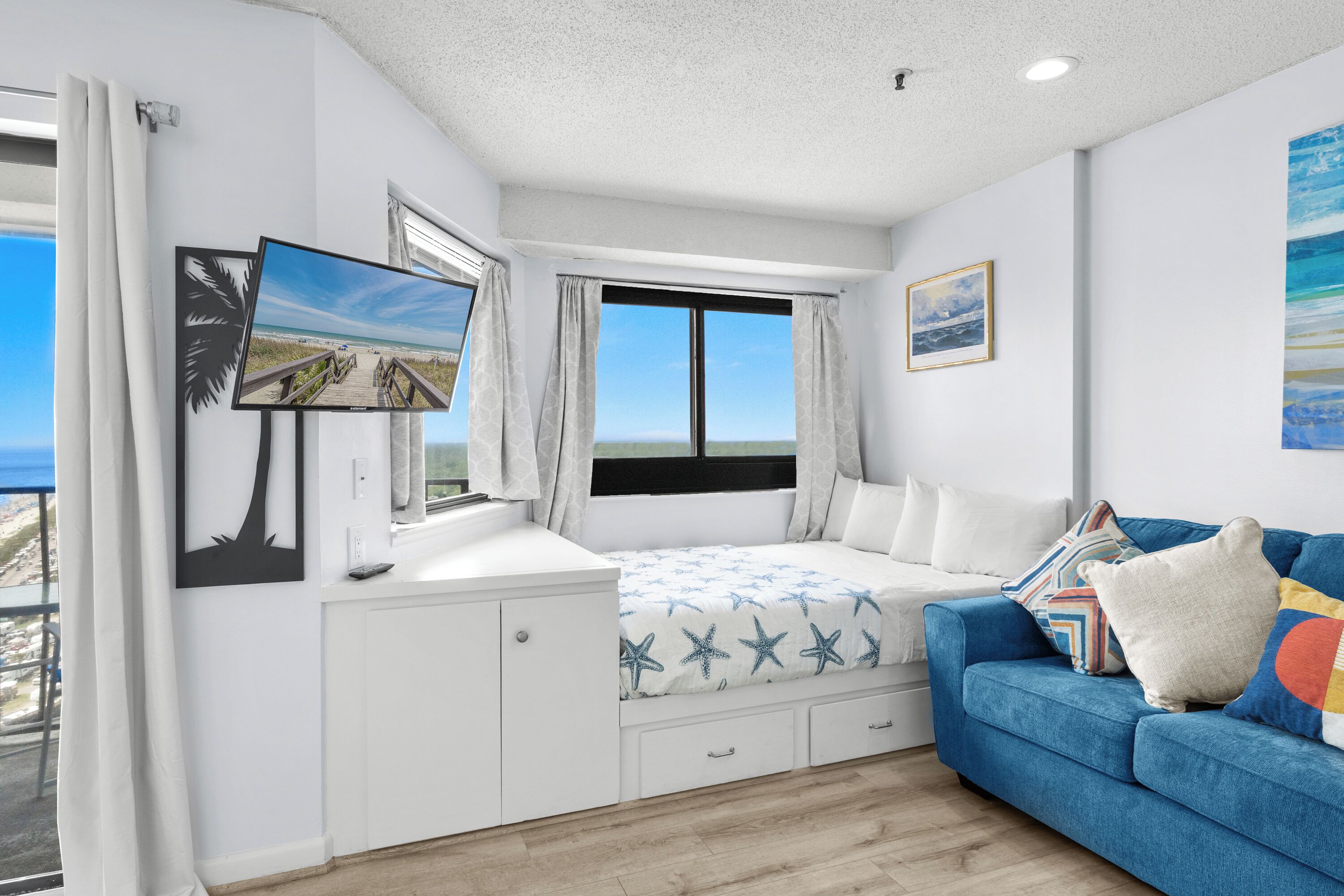 A bedroom with a bed, a blue sofa, a TV, and a painting.