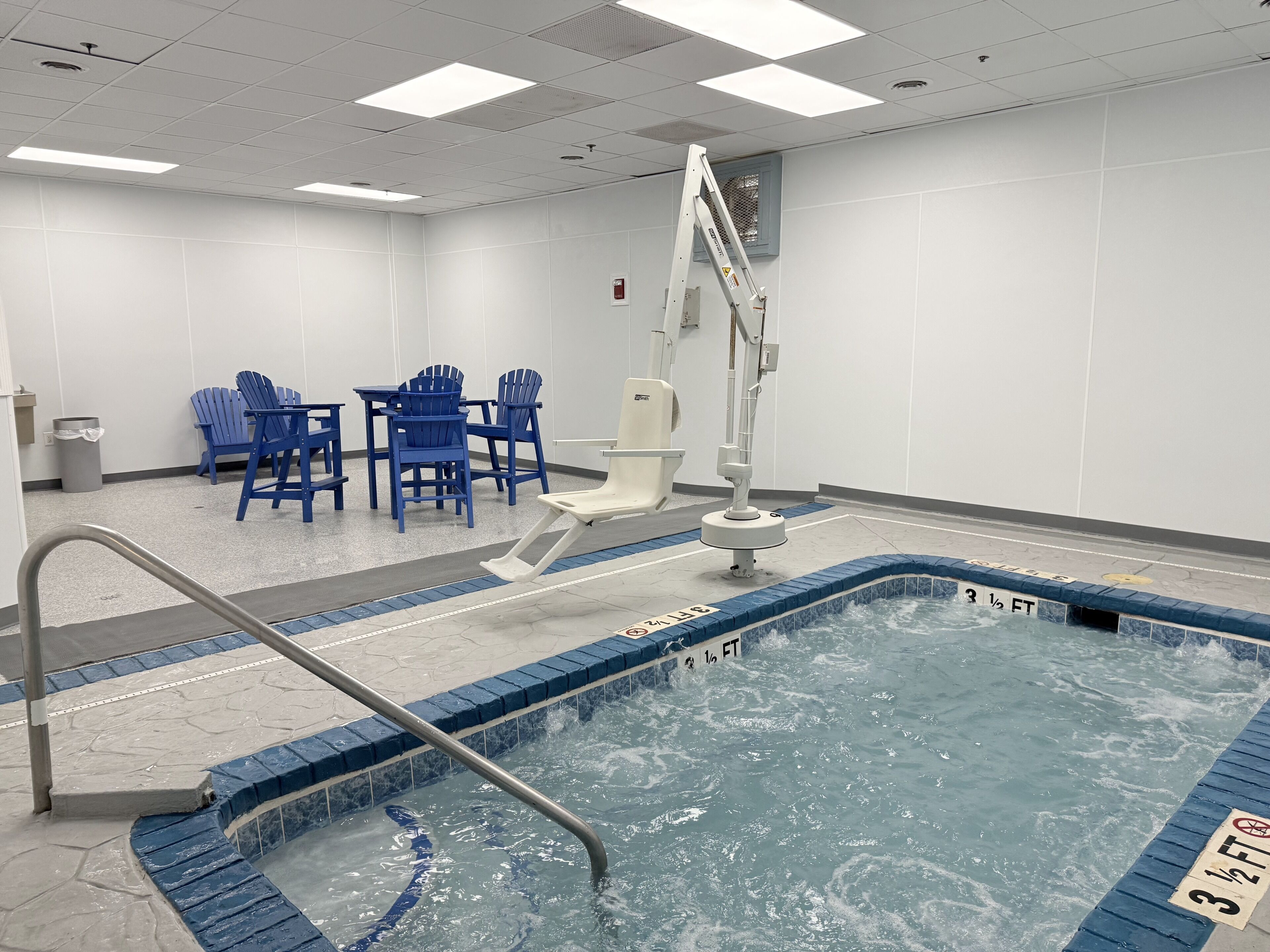 A swimming pool with a ladder, blue chairs, and a white toilet.