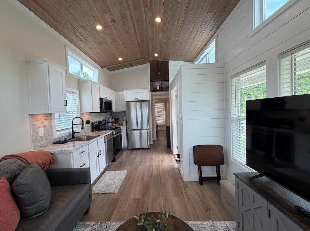 A modern kitchen with white cabinets, stainless steel appliances, and a wooden ceiling.
