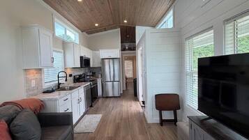 A modern kitchen with white cabinets, stainless steel appliances, and a wooden ceiling.