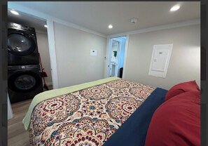 A bedroom with a bed, a washing machine, and a door leading to another room. - Magnolia Modern Tiny Home (Vicksburg)
