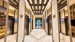Un pasillo de hotel con piso de mármol, ascensores y pantallas digitales que muestran información.