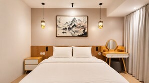 A modern hotel room with a large bed, wooden headboard, bedside tables, a desk with a mirror, and a wall-mounted painting.
