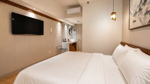 A hotel room with a large bed, a flat-screen TV mounted on the wall, a small kitchenette, and a painting on the wall. - Pristine Living at Tokyo Riverside PIK2 (Teluknaga)