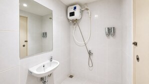Un baño moderno con un lavamanos blanco, un cabezal de ducha manual y una ducha empotrada en la pared.
