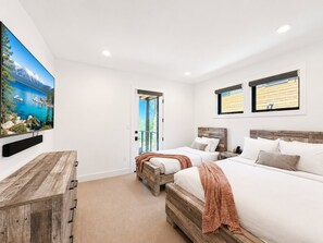 A bedroom with two beds, a TV, and a window with a view of a mountain and lake.