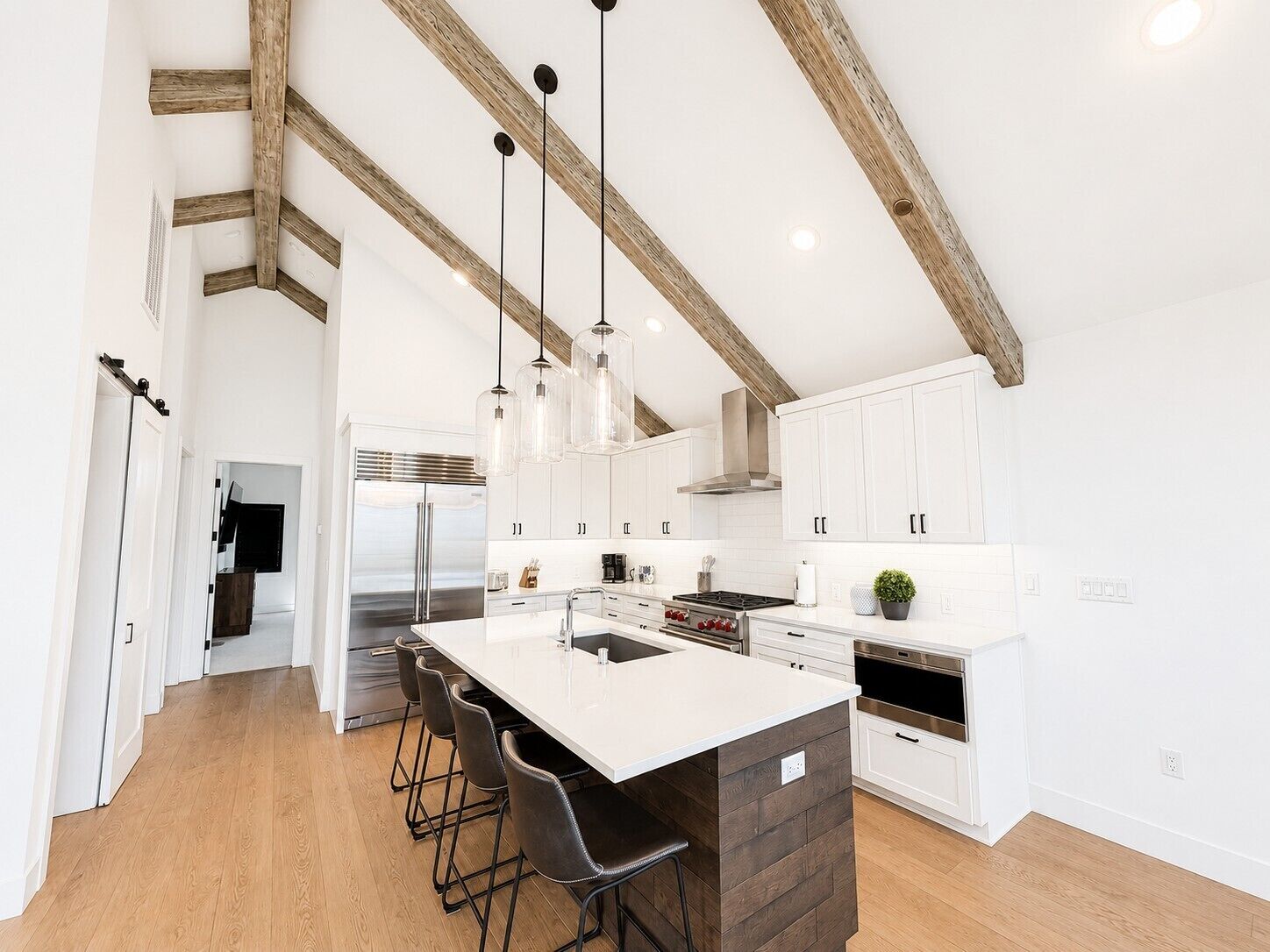 A modern kitchen with white cabinets, a central island with bar stools, and exposed wooden beams.