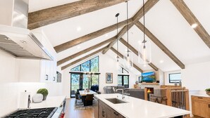 A modern kitchen with a large island, wooden beams, and a dining area with a view. - Firework Views from the Private Hot Tub, Luxury Sierra Colina Retreat (SC109) (Stateline)