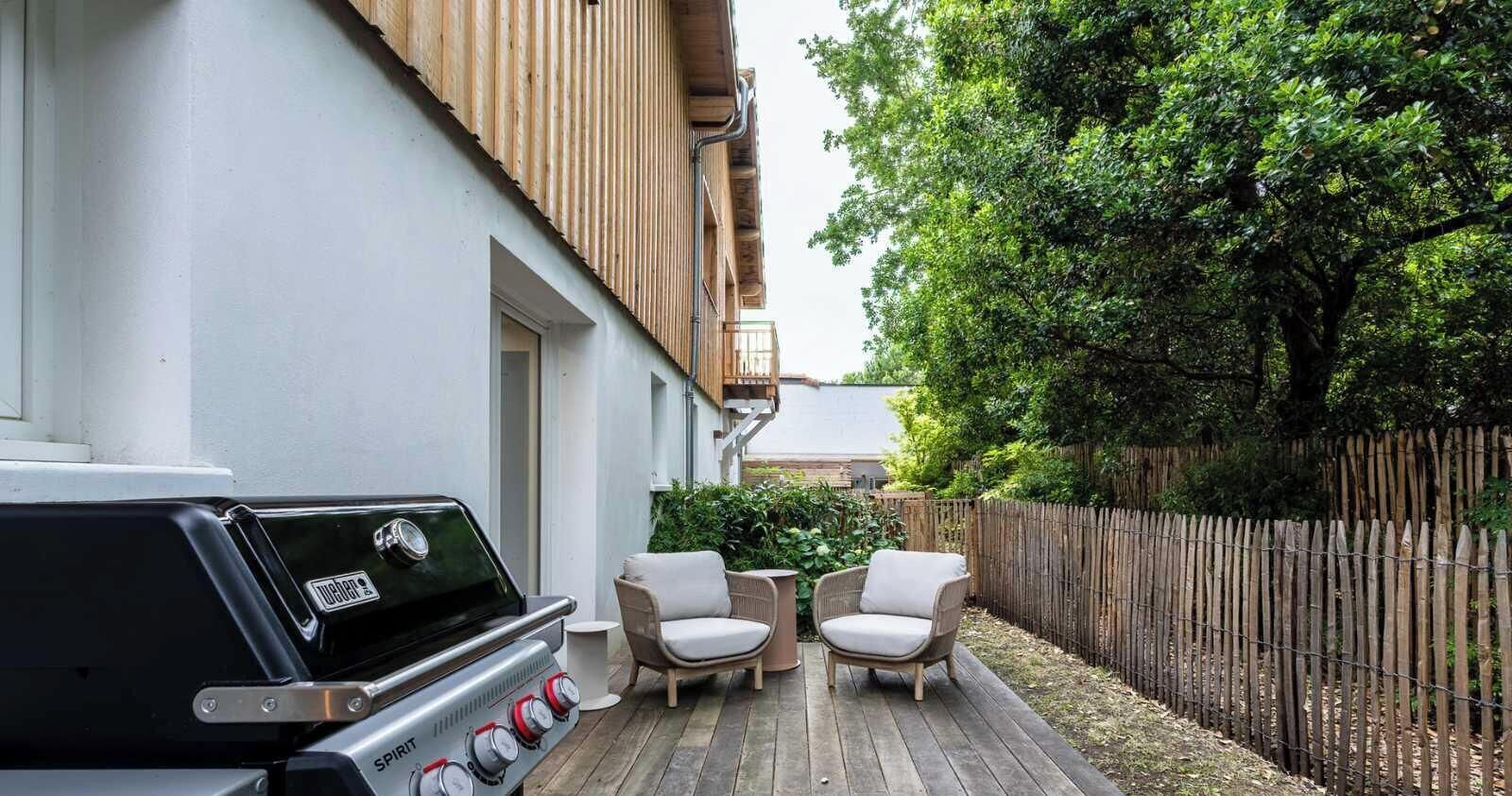 A barbecue grill, two wicker chairs, and a wooden deck.