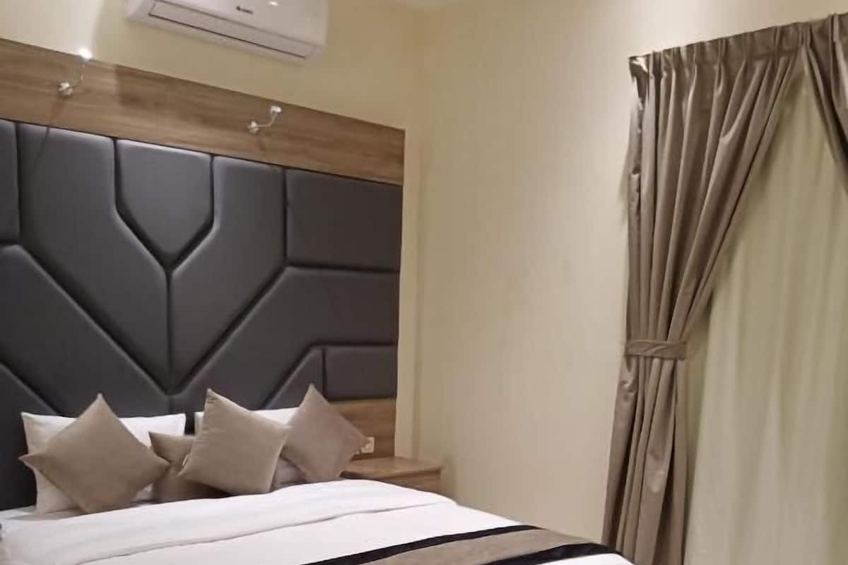 A bedroom with a bed, headboard, bedside table, and a window with curtains.