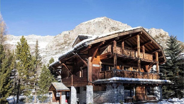 Eine Holzhütte mit Steinfundament, einem Balkon und einem Berg im Hintergrund.