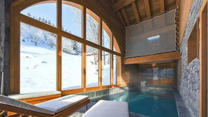 Ett spaområde med en pool, träbänkar och stora fönster med utsikt över ett snötäckt landskap.
