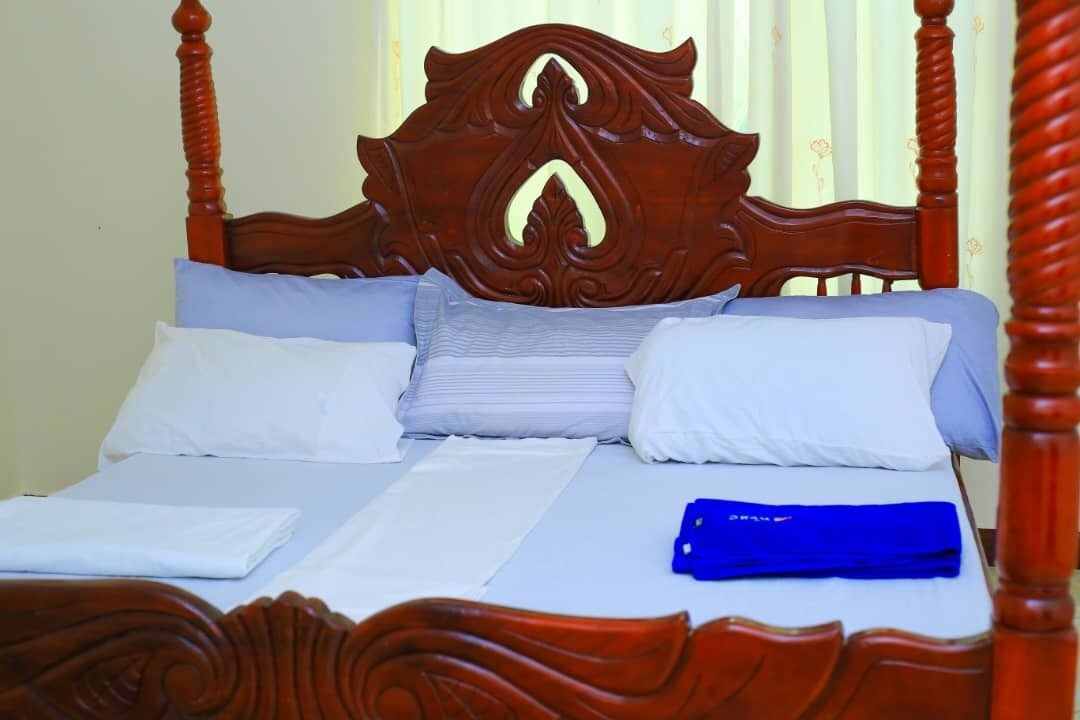 Un lit avec une tête de lit en bois, une literie blanche et un objet bleu posé sur le lit.