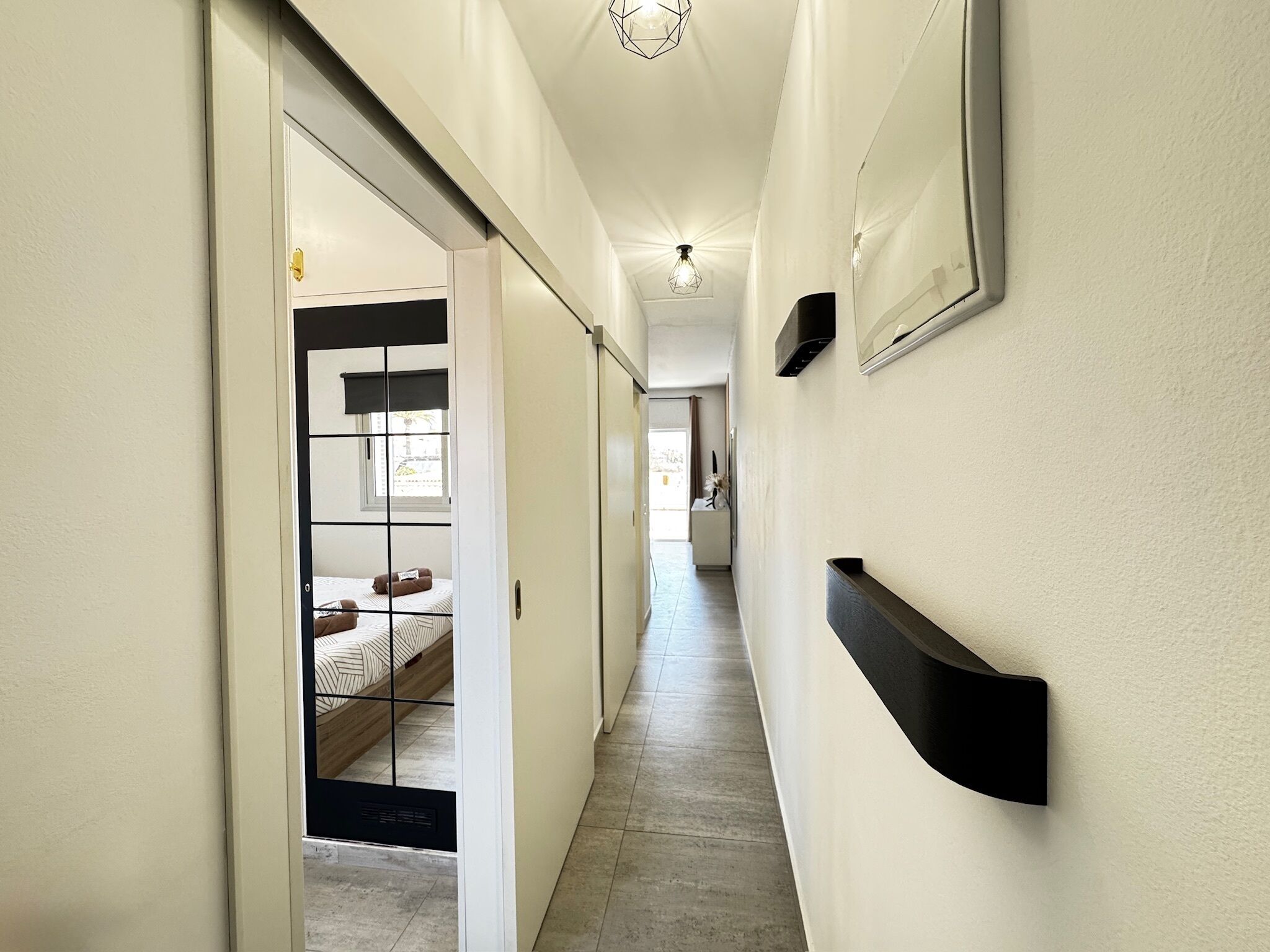 A hallway with a bed, a door, and a wall-mounted shelf.