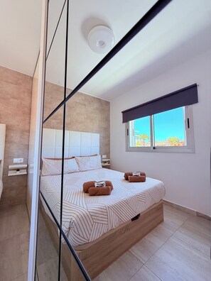 Ein modernes Schlafzimmer mit Bett, Nachttischen, einem Fenster und Blick nach draußen.