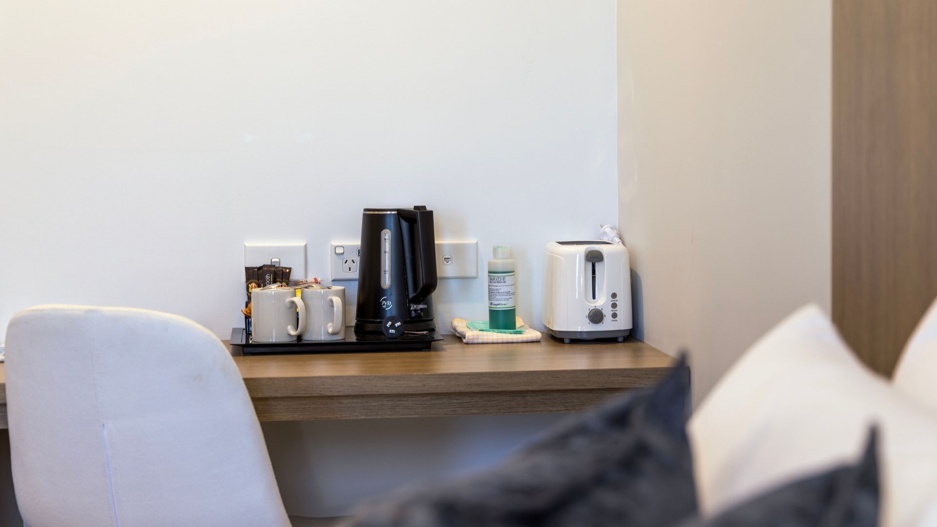 A hotel room with a wooden desk, a coffee maker, a toaster, and a bottle of hand sanitizer.