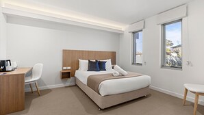 Een hotelkamer met een bed, nachtkastje, stoel, bureau en grote ramen.