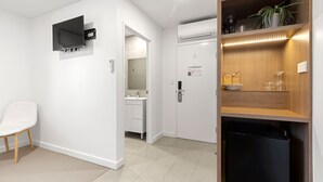 Een moderne hotelkamer met een flatscreen televisie, een ingebouwde airconditioning, een kleine koelkast en een houten plank met glazen.