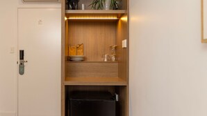 Een compacte kitchenette met een ingebouwde koelkast, een plank met keukengerei en een kleine plant.
