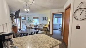 A kitchen with granite countertops, a coffee maker, a dining area with a table and chairs, a living room with a sofa, and a hallway leading to another room. - Aspen Cottage Ski In Ski Out 1BR at Lutsen Mtn (Lutsen)